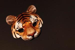 máscara de cara de máscara de rayas de tigre naranja con estampado realista de bozal de gato salvaje. máscara infantil de carnaval para fiestas navideñas. fondo marrón oscuro con espacio de copia. foto