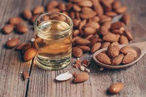 aceite de almendras y nueces de almendras en madera, delicioso aceite de almendras dulces en vidrio, nuez de almendra tostada para alimentos saludables y aceites vegetales orgánicos para refrigerios para cocinar o concepto de spa foto