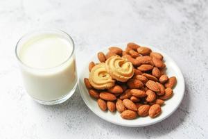 vaso de leche de almendras y galleta para el desayuno comida saludable - nueces de almendras en el fondo de la placa blanca foto