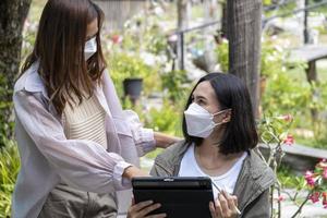 Two women discussing business while using a tablet. At a table in a cafe with a garden photo