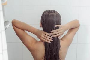 mujer joven lavando el cabello en la ducha. mujer asiática lavándose el pelo negro. foto