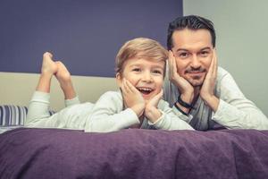 Portrait of happy son and father lying on the bed. photo