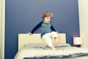 Playful boy in pyjamas jumping on bed. photo