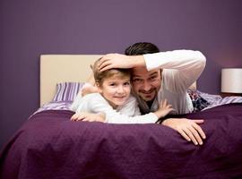 Cute kid and his father relaxing on the bed. photo