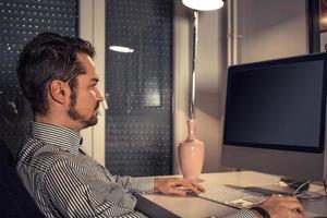 Businessman using desktop PC while working late in the office. photo