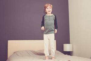 Happy boy jumping on the bed at home. photo