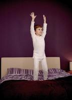 niño pequeño con los brazos levantados saltando sobre la cama. foto