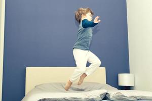 Active kid jumping high up on bed in the evening. photo