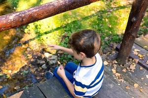 Above view of boy sitting on a bridge above the creek. photo