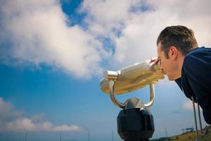 Man looking through coin operated binoculars against the sky. photo