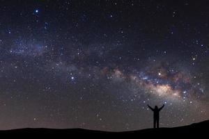 landscape with milky way, Night sky with stars and silhouette of a standing sporty man with raised up arms on high mountain. photo