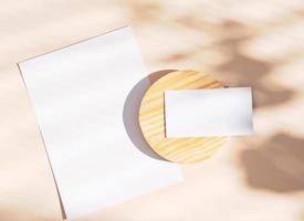 Flat lay of branding identity business name card and blank paper on yellow background, light and shadow shape leaves, minimal concept for design photo