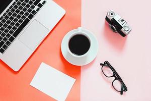 Living Coral color background, Color of the year 2019, flat lay of workspace desk with laptop, blank paper, coffee, eyeglasses and camera photo