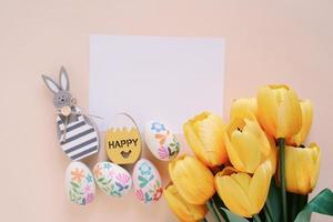 Happy Easter concept with blank card, wooden bunny, colorful easter eggs and yellow tulips. Top view with copy space photo