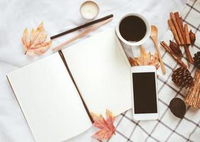 concepto de estilo de vida de otoño, cuaderno en blanco, teléfono inteligente y café con adornos de hojas de otoño sobre fondo de sábana blanca foto