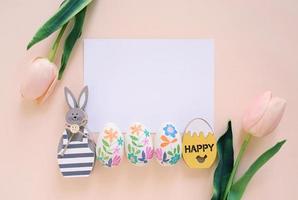 Happy Easter concept with blank card, wooden bunny, colorful easter eggs and pink tulips. Top view with copy space photo