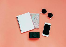 artículos de viaje concepto cuaderno en blanco, mapa, cámara, teléfono inteligente y gafas de sol sobre fondo amarillo, vista superior con estilo mínimo foto