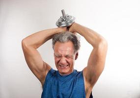 Mature Man 60plus working out with weights at home doing shoulder press with one arm photo