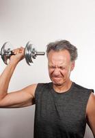 Mature Man 60plus working out with weights at home doing shoulder press with one arm photo