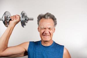 Mature Man 60plus working out with weights at home doing shoulder press with one arm photo