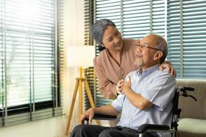 la pareja de ancianos se toma de la mano después de la jubilación, el esposo y la esposa se cuidan mutuamente en un momento romántico con una sonrisa feliz y disfrutan. abuelo asiático sentado en silla de ruedas mirando, copiando espacio foto