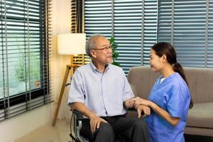 Asian Nurse take care Elderly Senior Man with warm welcome. 70s Mature Man patient has good health and support help by Caregiver from medical hospital. Grandfather sit on wheelchair, copy space photo