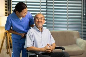 Asian Nurse take care Elderly Senior Man with warm welcome. 70s Mature Man patient has good health and support help by Caregiver from medical hospital. Grandfather sit on wheelchair, copy space photo