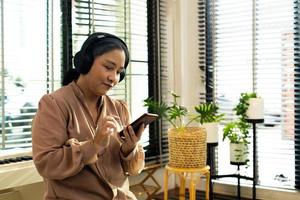 Grandmother listen old music in headphone near piano. Elderly Senior Asian woman enjoy relax from song wireless headset which play oldies songs as think old day and remember cool person, copy space photo