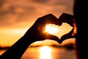 mano de silueta en forma de corazón con amanecer en el medio y fondo de playa foto