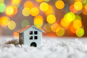 Abstract Advent Christmas Background. Toy model house on snow with defocused garland lights background. Christmas with family at home concept. Christmas winter composition. photo