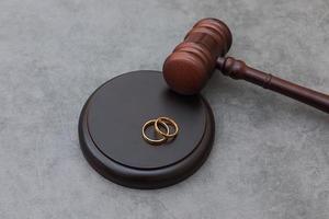 Law theme. Judge gavel wedding rings on concrete stone grey background. Divorce proceedings. Mallet of judge deciding on marriage divorce, marital agreement, legalities of divorce. photo