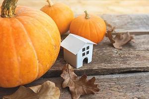 Autumnal Background. Toy house and pumpkin on wooden background. Thanksgiving banner copy space. Hygge mood, change of seasons concept. Hello Autumn with family Halloween party. photo