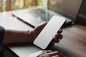 Mockup image of a man holding and using smartphone with blank desktop screen while working and drinking coffee in cafe. photo