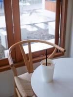 ice milk coffee in white plain empty paper cup on table near glass window in minimal japanese style cafe photo