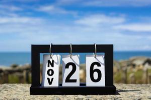 26 de noviembre texto de fecha de calendario en marco de madera con fondo borroso del océano. foto