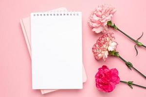 bloc de notas y flor de clavel rosa sobre fondo rosa foto