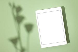 Blank screen tablet mock up and shadow on green pastel background. Copy space. Mock up template. Business communication. Isolated object. Spring decoration. photo