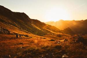 Man and woman hikers in distance hike on trail outdoors on beautiful sunset in autumn together against sun. Cinematic inspirational active people on trek in caucasus mountains photo