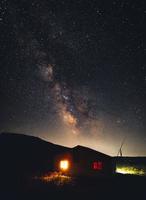 Nightscene of illuminated wooden house hut in mountains isolated with milky way starry night scene in summer