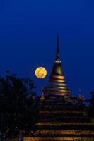 la superluna en el cielo nocturno y la silueta de la antigua pagoda se llama wat ratchaburana, phitsanulok en tailandia foto
