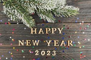 Happy New year 2023 celebration. Wooden text and numbers 2023 on wooden background with scattered golden confetti and fur tree branch photo