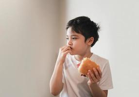 niño hambriento comiendo sándwiches caseros de tocino con verduras mixtas, niño sano desayunando en casa, niño mordiéndose las uñas y mirando con cara pensante foto