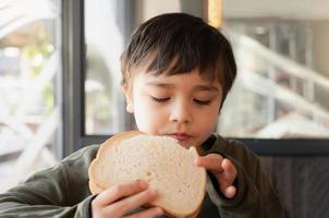 Portrait healthy young boy eating bacon sandwich, School Kid having breakfast in the cafe be for go to school, Child bitting toast sandwich beef cheddar cheese for lunch. photo