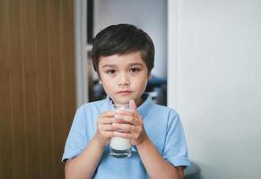 Portrait healthy school boy drinking glass of milk for breakfast, Happy child standing in kitchen drinking warm milk before go to school. Healhty food liftstyle concept photo