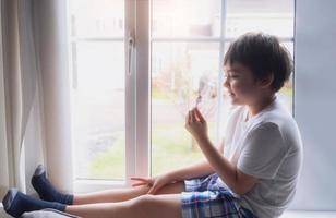 A Happy kid eating some ice cream, Portrait of a handsome young boy sitting next to a window having a refreshment, Child with a smiling face relaxing at home. Kid looking at camera photo