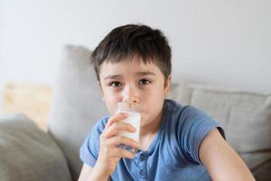 Portrait healthy school boy drinking glass of milk for breakfast, Happy child sitting on sofa drinking warm milk before go to school. healthy food lifestyle concept photo
