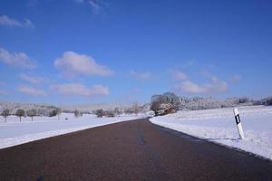 un camino en invierno en Baviera conduce a través de un paisaje nevado contra un cielo azul foto