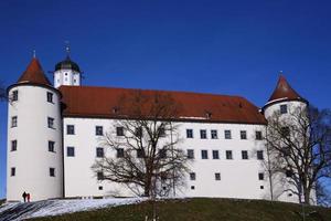 el histórico castillo de hoechstaett se alza sobre una colina frente a un cielo azul, detrás de árboles desnudos, bajo el sol foto
