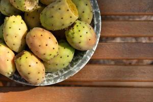 Several ripe prickly pear fruits lie in a ceramic bowl. The bowl stands on a base made of rustic wood. There is space for text. photo