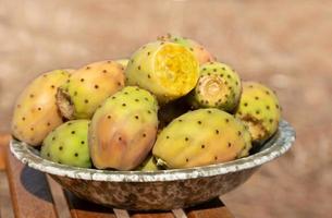 Several ripe prickly pear fruits lie in a ceramic bowl. The bowl stands on a base made of rustic wood. photo